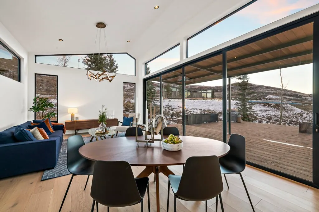 Icon Haus — vaulted dining room opening through black-framed glass doors to the deck