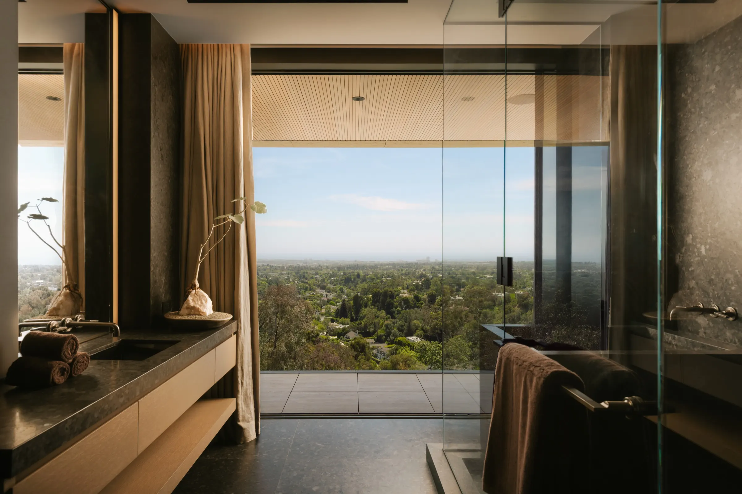 The Getty House, Brentwood — primary bath in dark stone with the view beyond