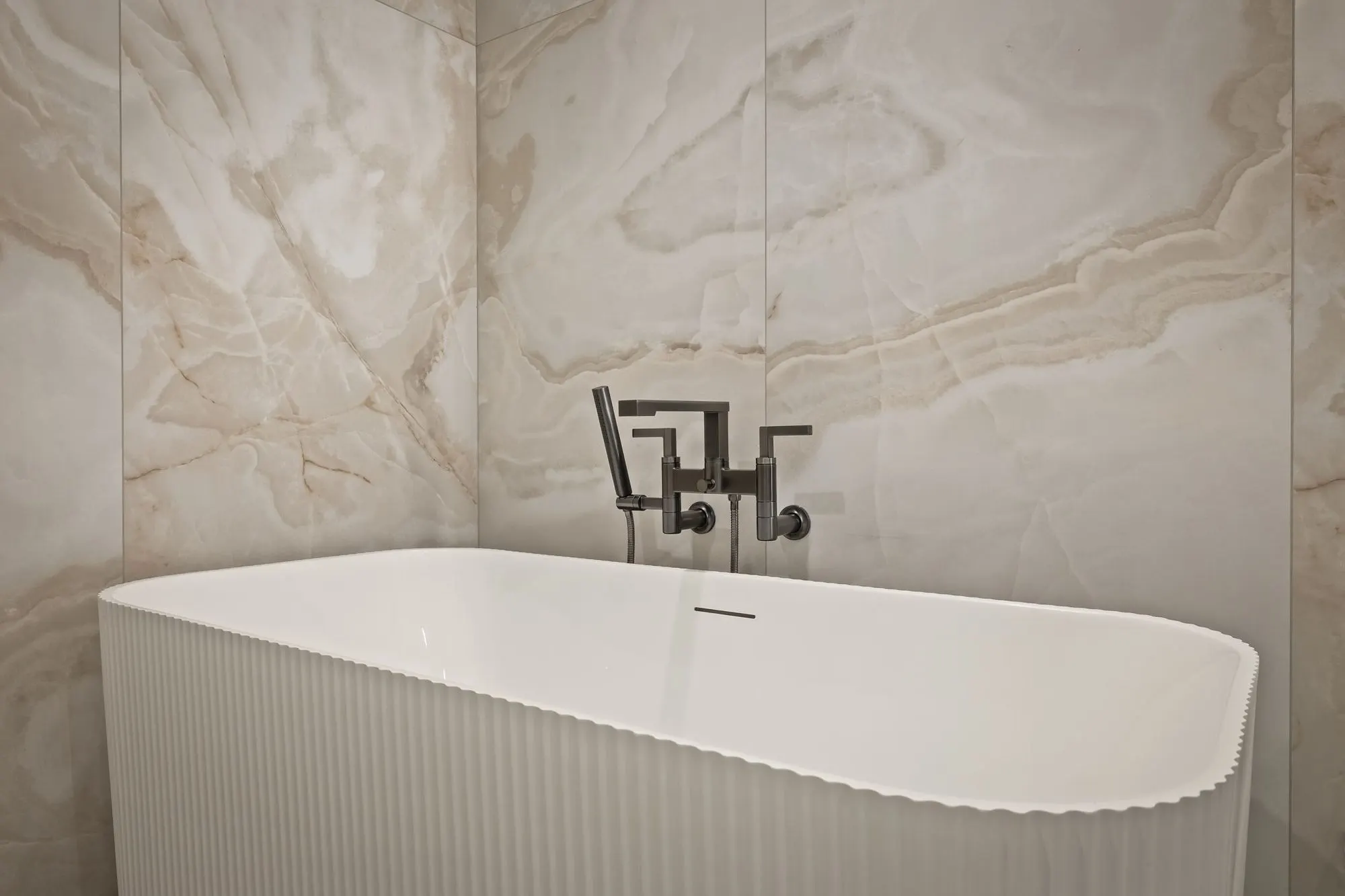 Lumen — freestanding tub against book-matched stone in the primary bath