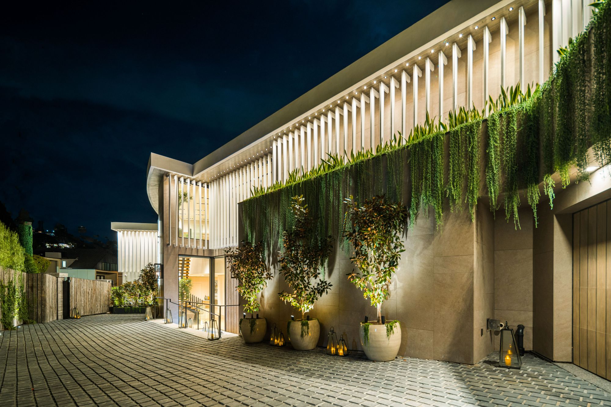 Flicker Estate — entry façade at night, louvered screens and hanging gardens