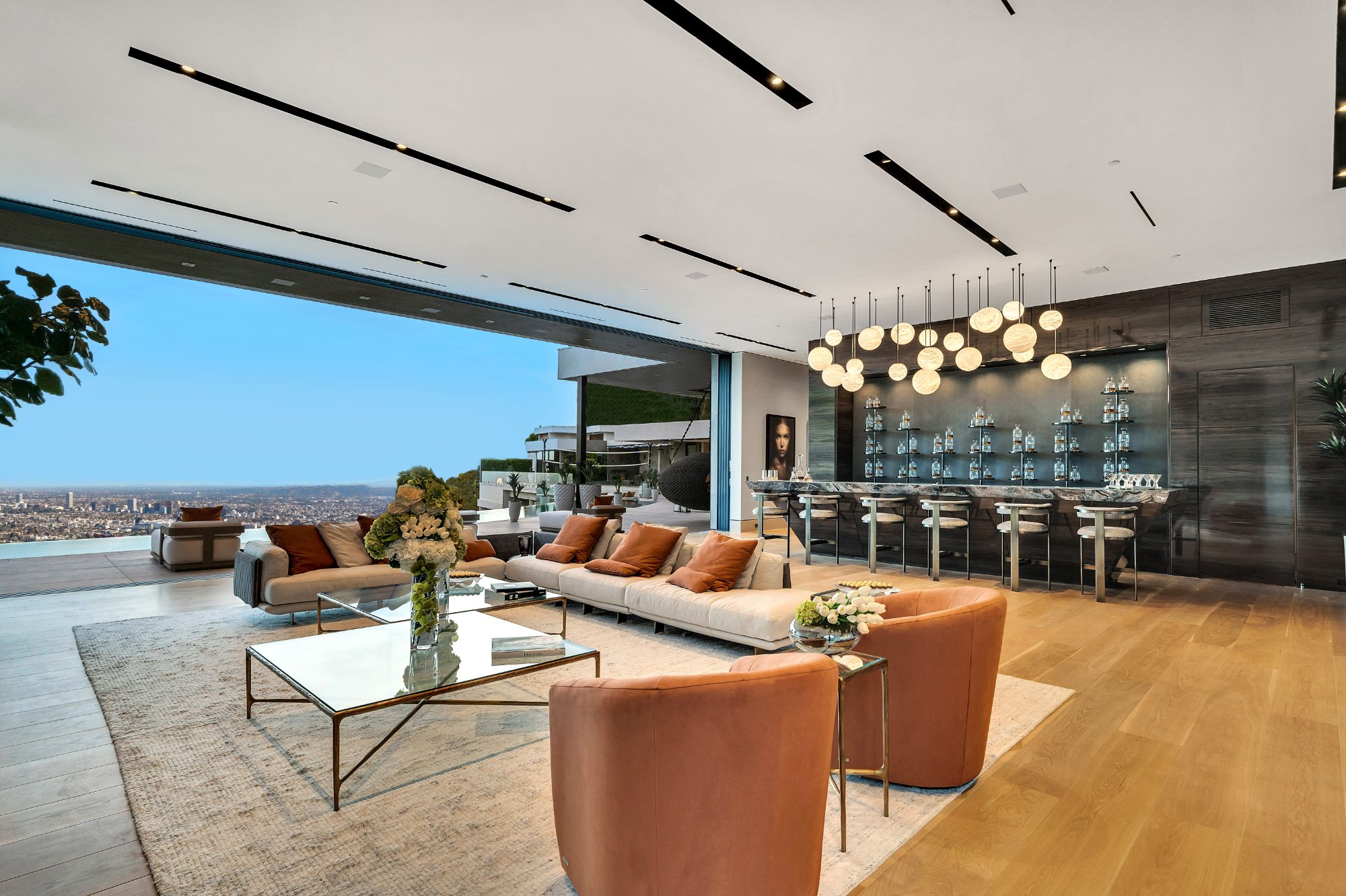 Flicker Estate — living room and bar under the brass pendant cluster, city beyond