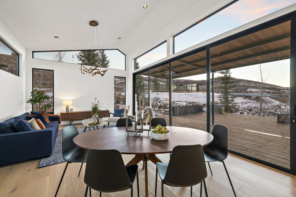 Icon Haus — vaulted dining room opening through black-framed glass doors to the deck