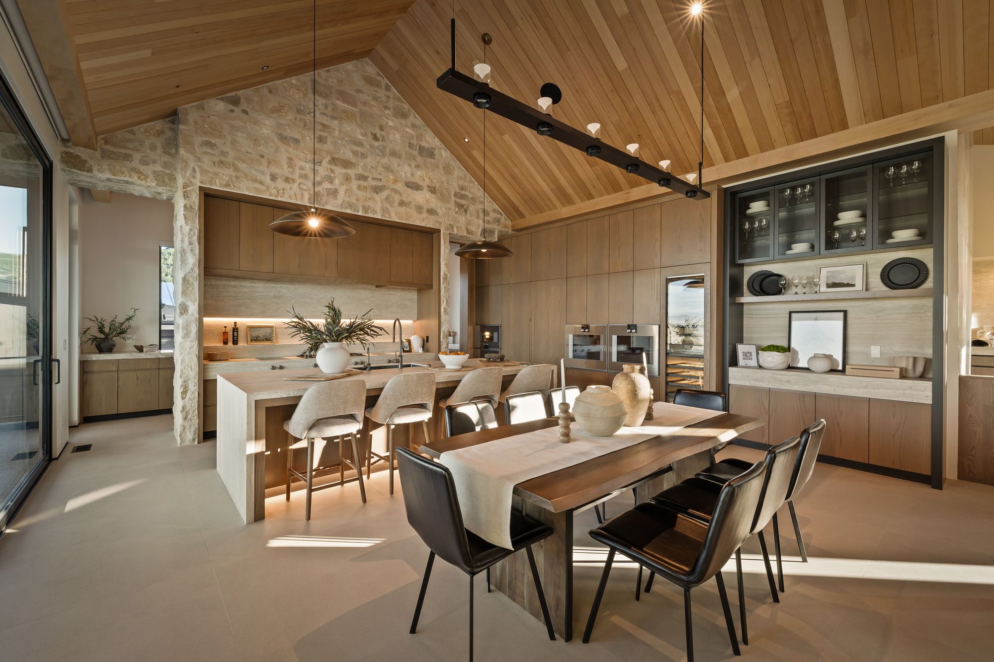 Lumen dining and kitchen under a vaulted ceiling with a glass wall